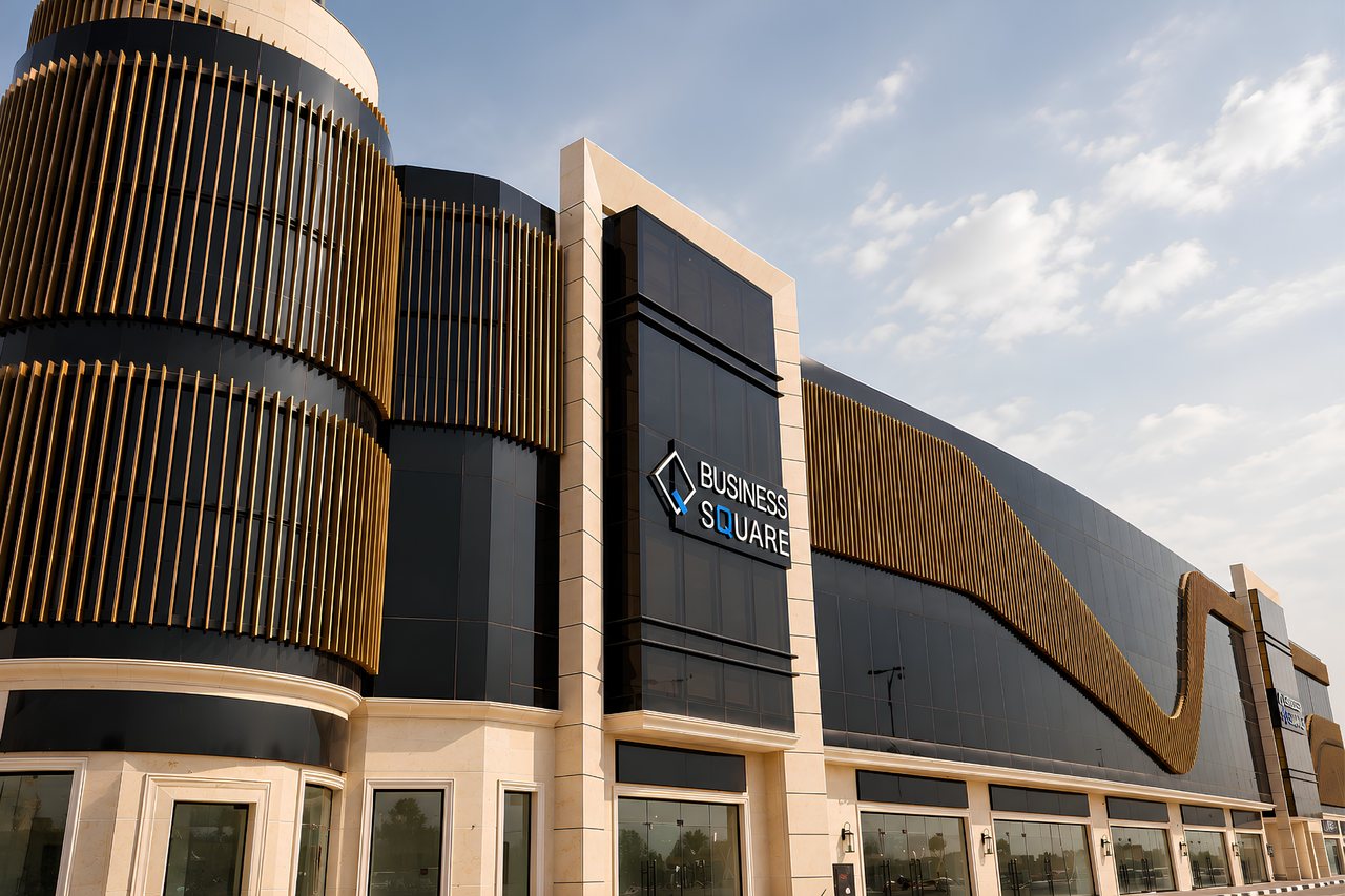 The curved corner tower of Business Square clad in vertical champagne fins against a clear Ajman sky