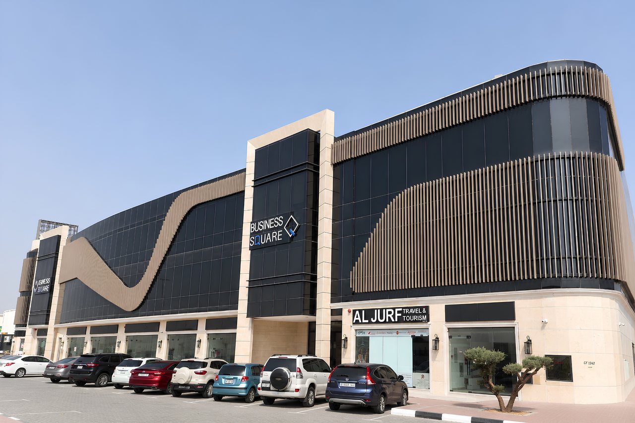Business Square street elevation on Sheikh Ammar Bin Humaid Street, showing the bronze fin façade and ground-floor retail units