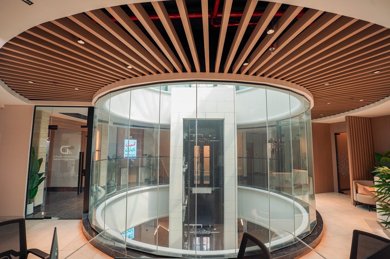 The glass capsule lift at the heart of the Business Square lobby beneath a radial timber ceiling